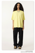 Female model wearing pale yellow oversized t-shirt with black wide-leg pants, styled with silver chain necklace and beige footwear against white background