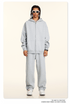 Model wearing light gray oversized zip-up hoodie and matching sweatpants with white rectangular sunglasses and silver chain necklaces against cream background