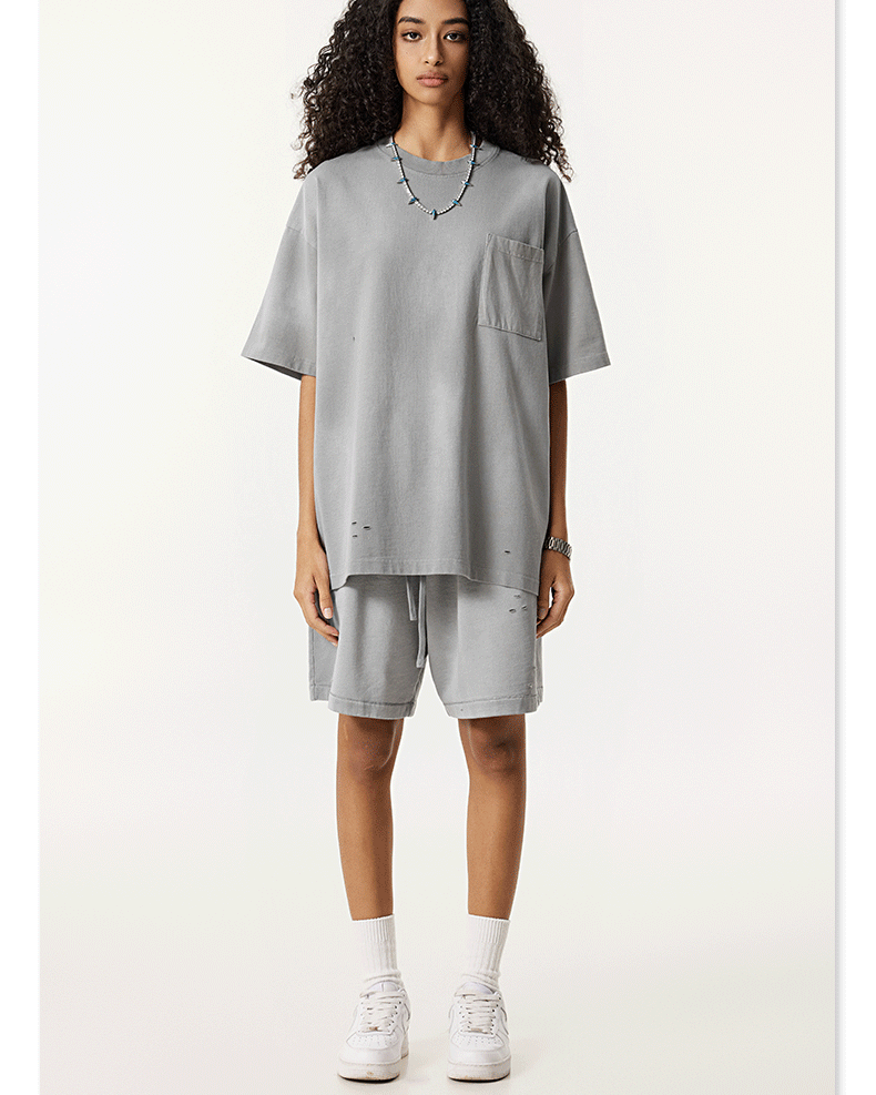 Model with curly hair in light gray t-shirt and shorts set, white sunglasses and sneakers against neutral backdrop