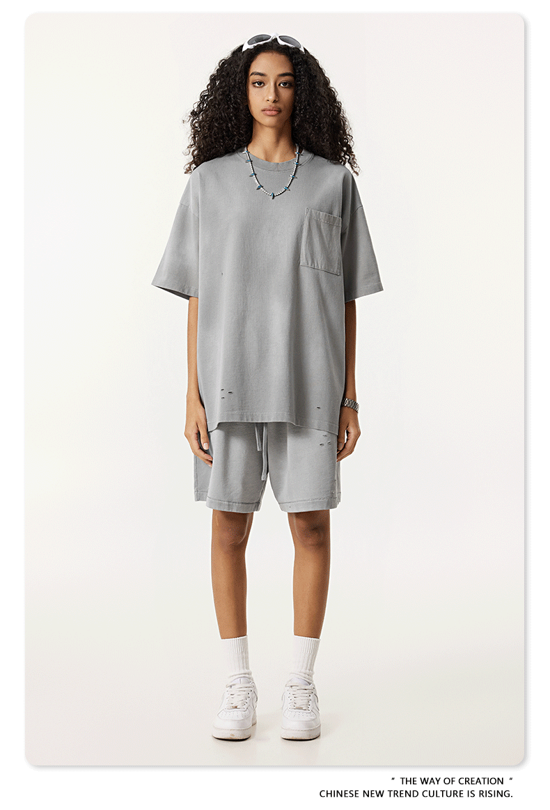 Model with curly hair in light gray t-shirt and shorts set, white sunglasses and sneakers against neutral backdrop