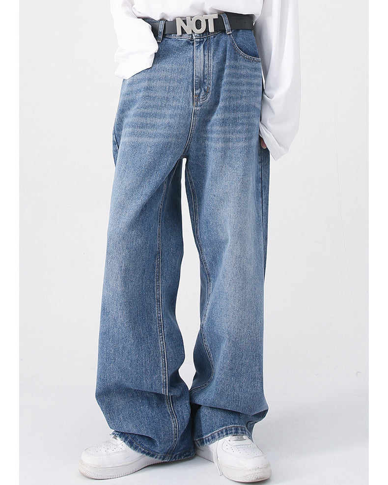 A model wears blue wide-leg jeans with a black "NOT" belt, a white long-sleeve shirt, and white sneakers, posing casually