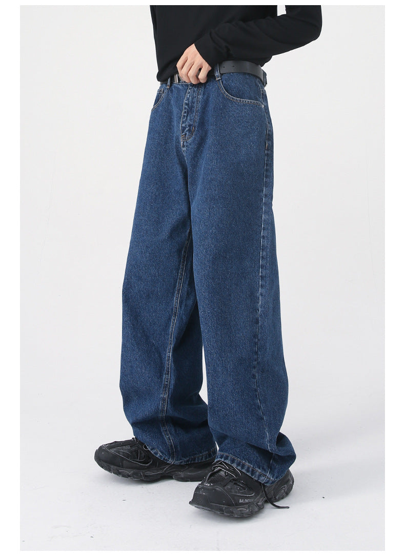 A side view of dark blue wide-leg jeans, showing their oversized fit, worn with a black shirt, "NOT" belt, and black sneakers
