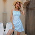 Woman wearing a blue floral spaghetti strap dress with a straw hat, posing outdoors against a wooden door