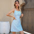 Woman in a blue floral summer dress with thin straps, posing with one hand on her hip against a neutral background