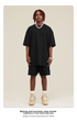 Model with dreadlocks wearing black oversized t-shirt and matching shorts with silver chain necklace and cream sneakers against cream background