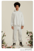 Man with afro in light gray hoodie and pants set wearing silver chain necklace among pink flowers