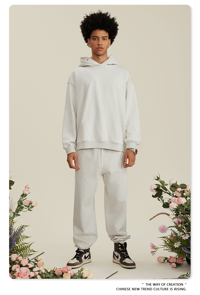 Man with afro in light gray hoodie and pants set wearing silver chain necklace among pink flowers