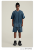 Model with short locs wearing navy blue t-shirt and shorts set with silver chain necklace, white socks and black sneakers against cream background