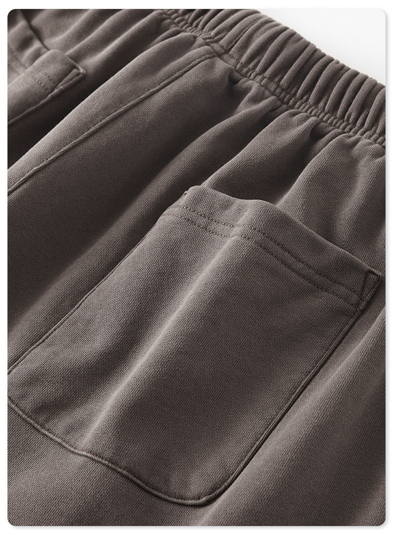 Detail shot of charcoal gray sweatpants fabric with elastic waistband and patch pocket visible on white background