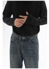 A close-up of a model wearing dark-wash wide-leg jeans and a black ribbed sweater, with hands visible adjusting the sleeve