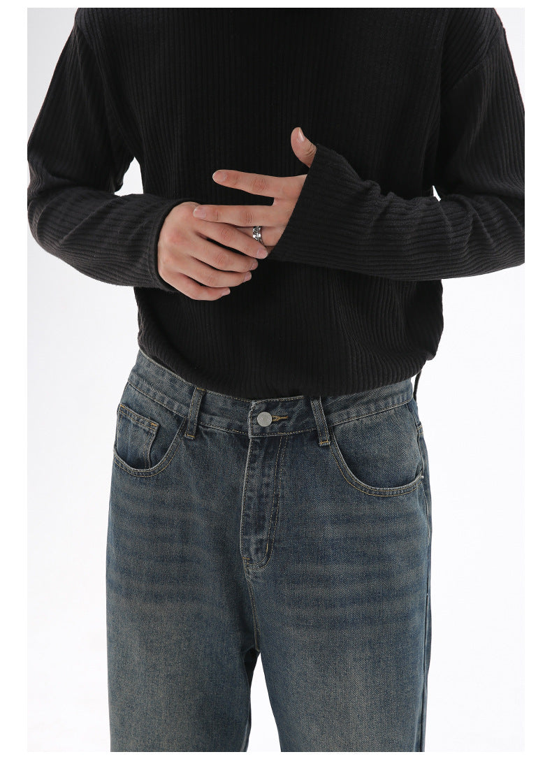 A close-up of a model wearing dark-wash wide-leg jeans and a black ribbed sweater, with hands visible adjusting the sleeve