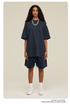 A woman with curly hair wearing a navy oversized t-shirt and matching shorts set, styled with white socks, sneakers, and a pearl necklace