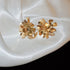 Gold Cluster Flower Earrings – Intricate gold floral earrings with multiple layers of delicate, petal-shaped elements, set against satin fabric