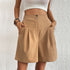 Model wearing khaki high-waisted pleated shorts with white crop top and layered bracelets against textured white wall