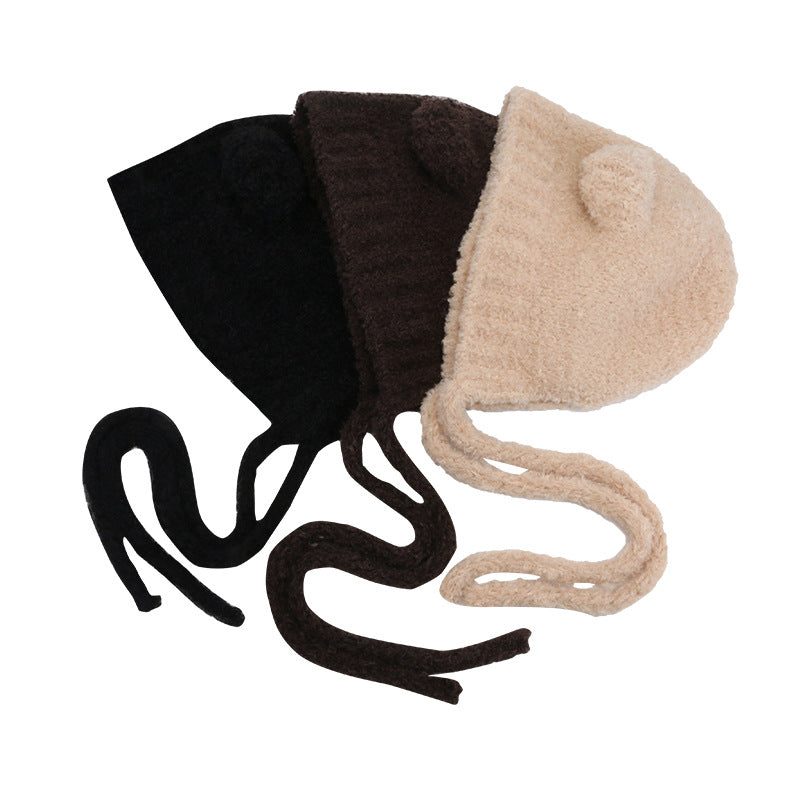 Three plush bear ear bonnets with tie closures in black, brown and beige colors arranged against white background on brown setting