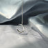 Delicate silver crescent moon necklace suspended against silvery fabric with shadow effect