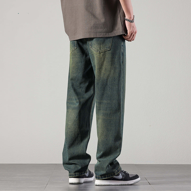 A rear view of a man wearing baggy greenish-blue denim jeans with visible fading and back pockets, paired with sneakers