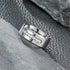  A polished silver-tone men's ring featuring a row of cubic zirconia, resting on a black background with a luxurious finish.