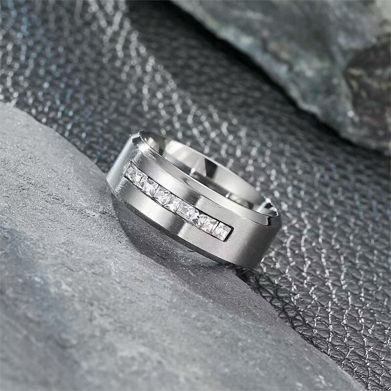  A polished silver-tone men's ring featuring a row of cubic zirconia, resting on a black background with a luxurious finish.