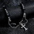A detailed shot of a black faceted bead bracelet with silver chain accents and a cross pendant, elegantly draped over a black leather surface.