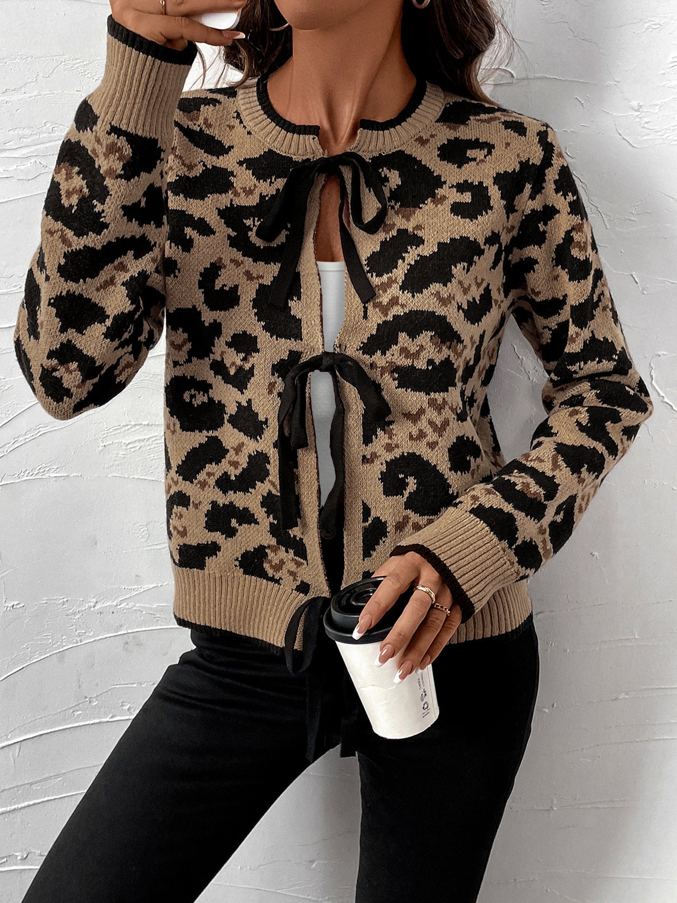 Model holding coffee cup, wearing tan and black animal print cardigan with front ties, black pants