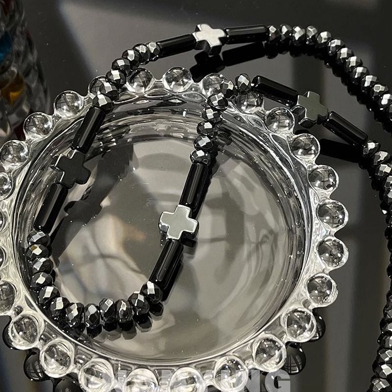 Close-up of silver necklace featuring black beads and decorative crosses on dark surface