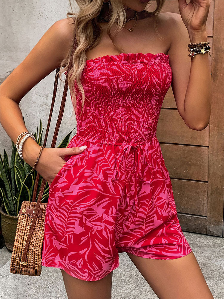 Woman wearing a red strapless romper with pockets, accessorized with bracelets and a woven handbag.