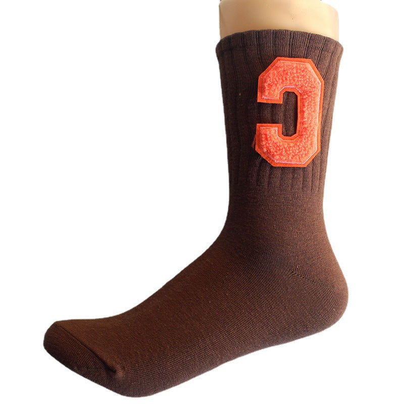 A model is wearing a brown varsity-style crew sock with a textured orange "C" patch, displayed on a mannequin leg against a plain white background