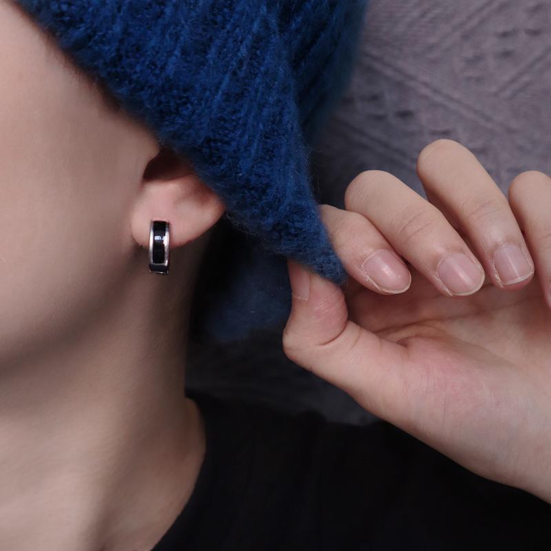 Close-up of silver and black huggie hoop earring worn with blue sweater