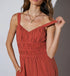A close-up of the ruched bust and adjustable straps of a rust-colored jumpsuit, highlighting the fabric texture.