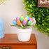 A single white ceramic pot featuring a cluster of artificial speckled eggs in pink, blue, green, and yellow, placed on a wooden surface with greenery.