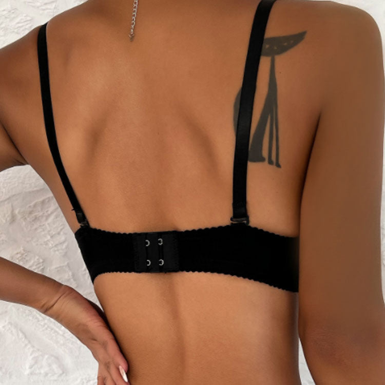 Back view of a black bra with adjustable straps and hook closure, showing tattoo on model's shoulder against white textured background