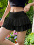 Side view of black high-waisted ruffle mini skirt with fitted waistband, shown against lush garden foliage