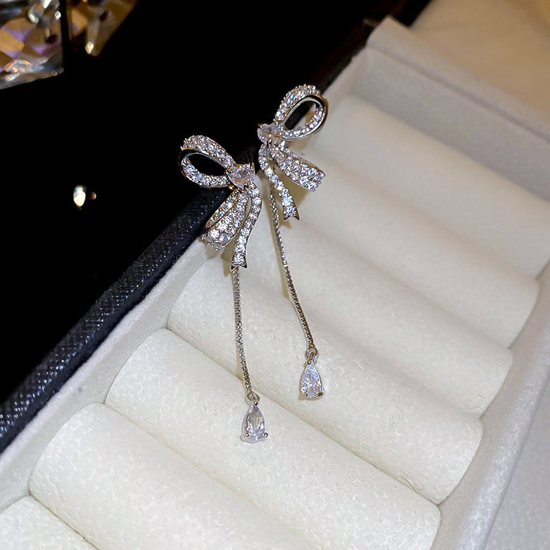 Silver bow drop earrings nestled in white cushioned jewelry box, showing elegant chain pendant design