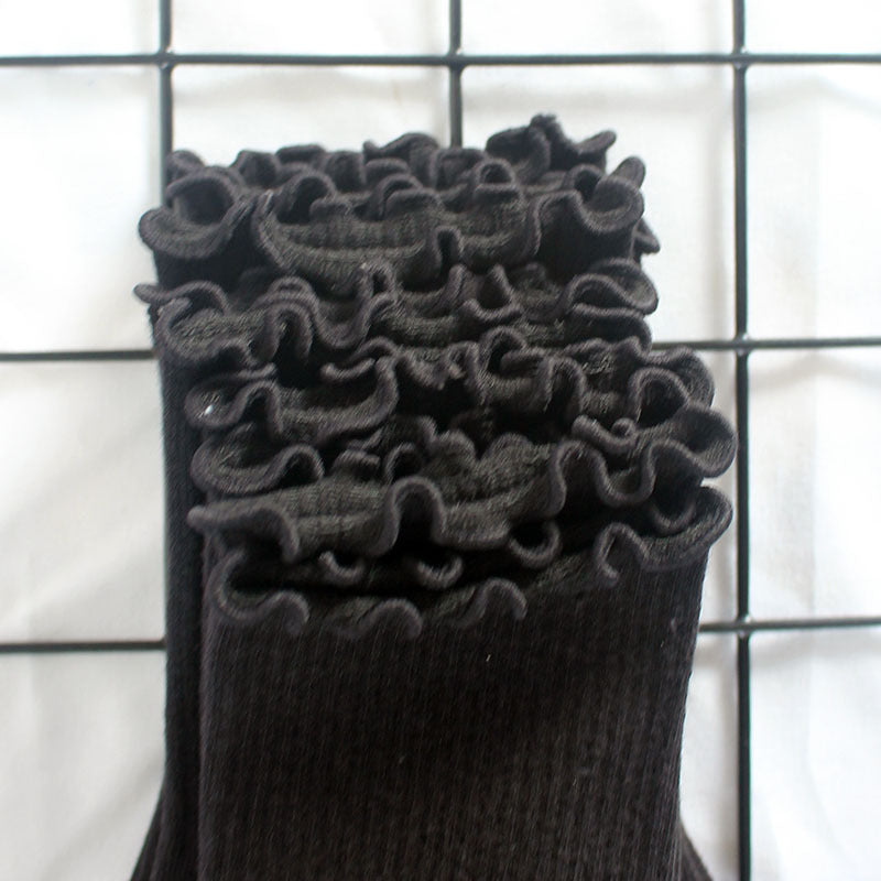 Close-up of black ankle sock showing detailed ruffled edge trim and ribbed texture, displayed on metal grid against white background