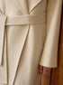 Detail shot of coat's tie belt and clean finishing on cream wool fabric