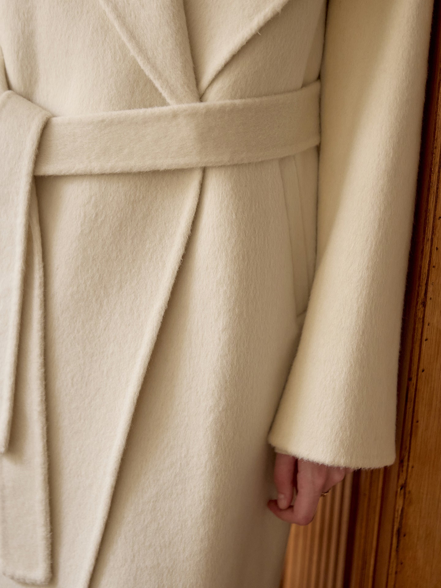 Detail shot of coat's tie belt and clean finishing on cream wool fabric