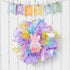 Pastel Easter wreath with mesh ribbons and bunny decoration, displayed on a white wooden background.