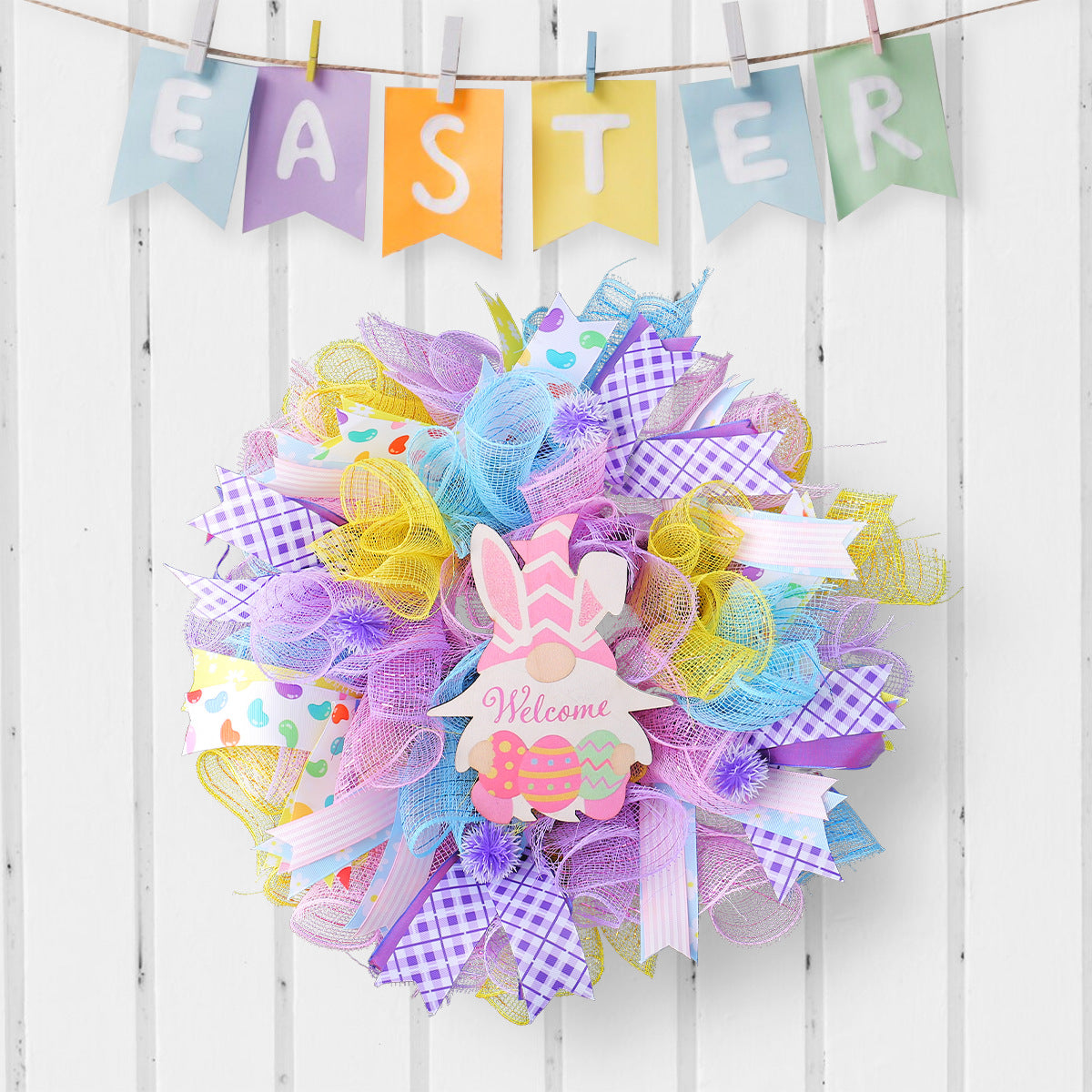 Pastel Easter wreath with mesh ribbons and bunny decoration, displayed on a white wooden background.