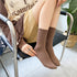 A woman sitting in a chair wearing brown ribbed crew socks with beige outfit, white sneakers, and displaying silver rings