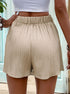 Close-up of elastic waistband detail on beige pleated shorts with flowing silhouette, styled with white crop top