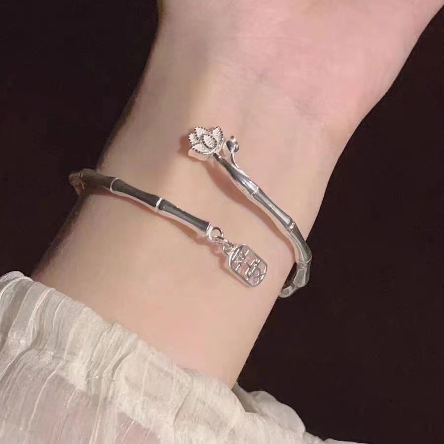 A silver adjustable bracelet with flower design and lucky charm worn on wrist with white sleeve details