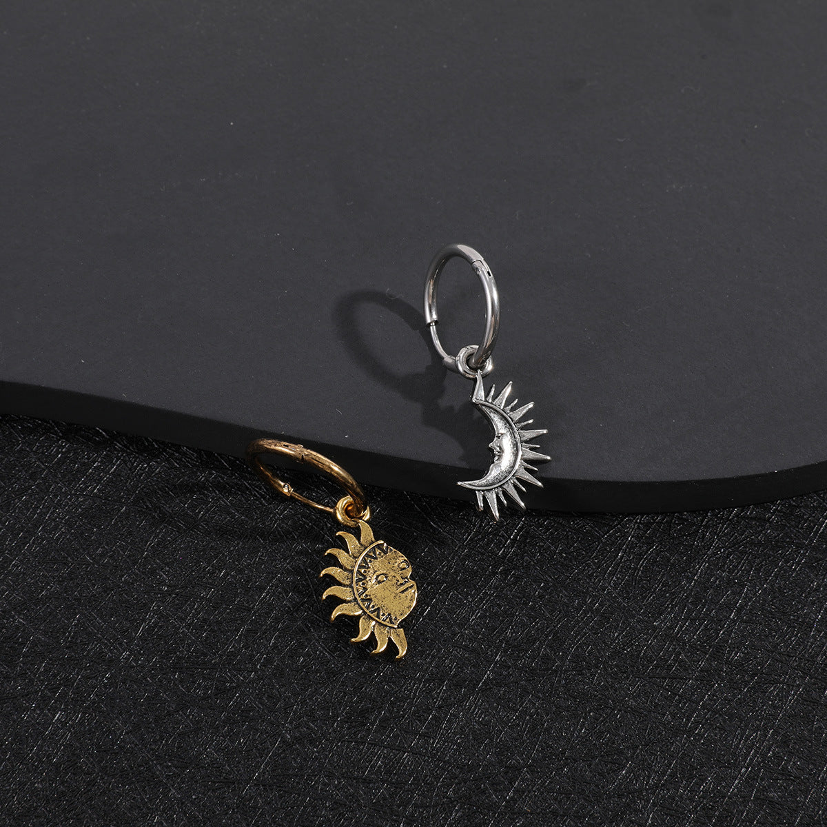 Gold sun and silver moon ear charms on black surface