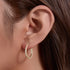 A woman wearing gold crystal-encrusted hoop earrings with her brown hair cascading alongside. The earring sits perfectly against her ear