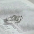 A delicate silver ring featuring a rose blossom with twig-like band resting on a printed book page, photographed in close-up