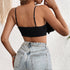 Back view of a woman wearing a black crop top with thin adjustable straps and smocked detailing, paired with denim jeans.