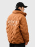 Side profile of man in camel brown Aesthetic quilted jacket showing back text detail and logo branding against white background