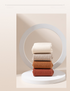 Four pairs of ribbed cotton socks stacked on circular white pedestal in white, beige, camel, and rust colors