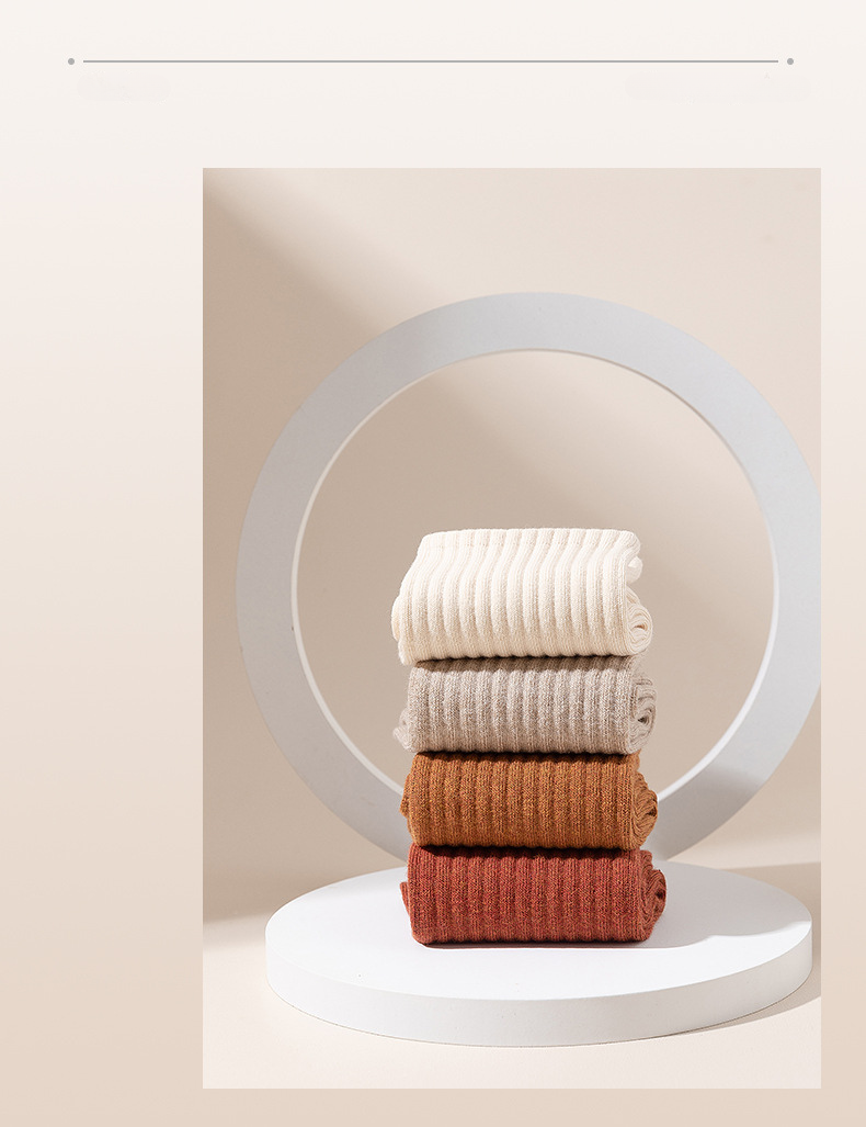 Four pairs of ribbed cotton socks stacked on circular white pedestal in white, beige, camel, and rust colors