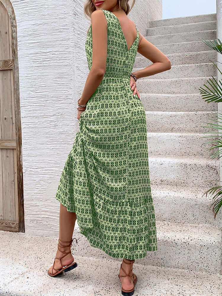 Back view of a woman wearing a green printed V-neck sleeveless maxi dress with a fitted waist, walking up white stone stairs.